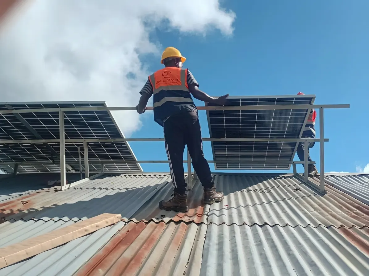 Technician in a hard hat, hi-vis vest and safety boots installing solar panels on a clinic roof